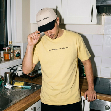 Model wearing the Black and Natural Don't Apologize for Being You embroidered hat with the Butter Comfort Colors tee