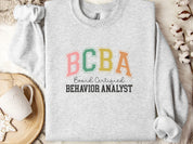 BCBA - Board Certified Behavior Analyst College Style Sweatshirt-Ash-Neurodiversity, ADHD & Autism Awareness & Acceptance Sweatshirt by Daily Bloom