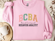 BCBA - Board Certified Behavior Analyst College Style Sweatshirt-Light Pink-Neurodiversity, ADHD & Autism Awareness & Acceptance Sweatshirt by Daily Bloom