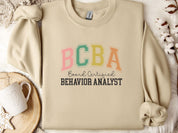 BCBA - Board Certified Behavior Analyst College Style Sweatshirt-Sand-Neurodiversity, ADHD & Autism Awareness & Acceptance Sweatshirt by Daily Bloom