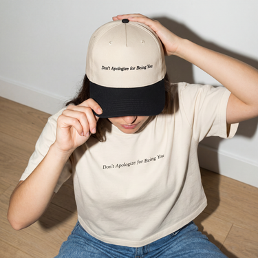 Model wearing the Black and Natural Don't Apologize for Being You embroidered hat with the Ivory boxy tee